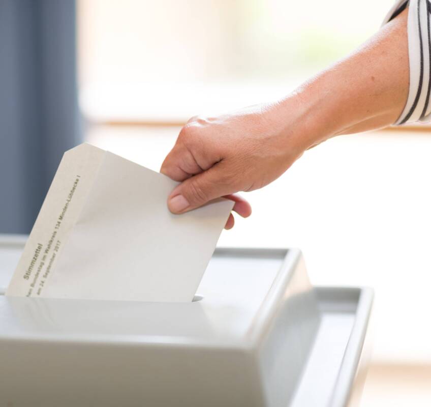 Wahlschein wird von Hand in Wahlurne eingeworfen
